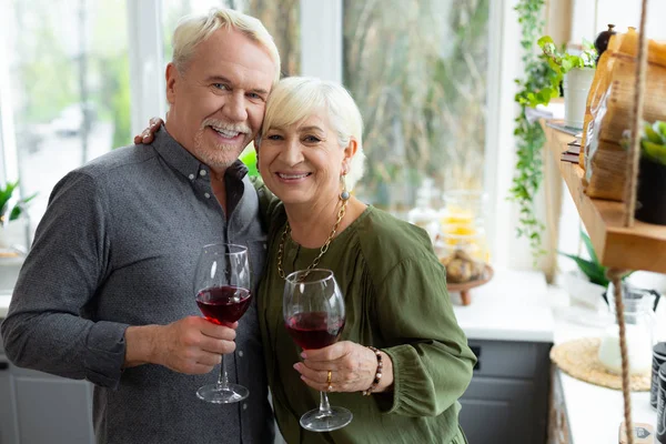 Веселые седовласые супруги обнимаются и держат бокалы с красным вином . — стоковое фото