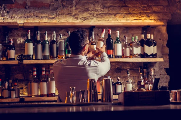 Бизнесмен берет бутылку коньяка, стоя у стойки бара — стоковое фото