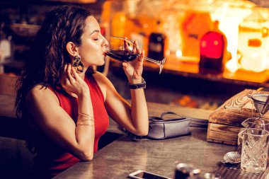Kırmızı elbiseli kadın barda oturuyor ve tek başına içiyor.