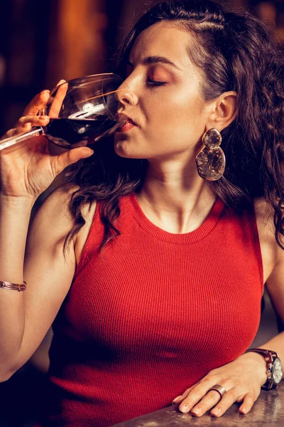 Close up of curly woman wearing red dress drinking red wine — Stock Photo, Image