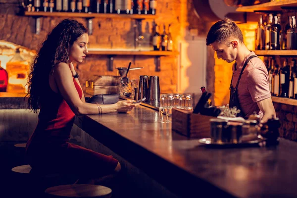Mulher de cabelos escuros em vestido vermelho esperando por sua bebida no bar — Fotografia de Stock