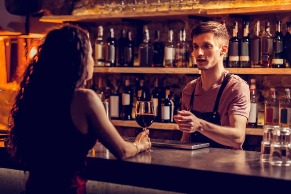 Barman talking to woman sitting at bar counter and drinking