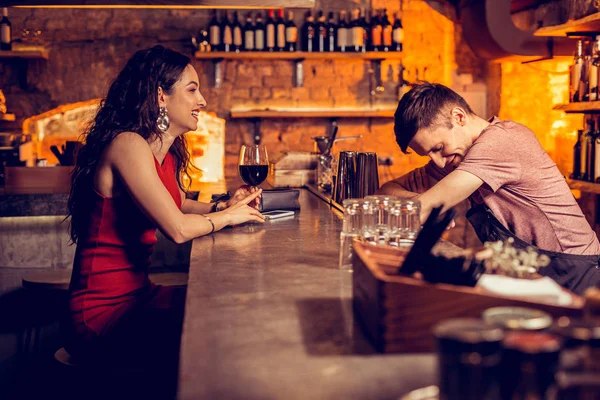 Кудрявая женщина в красном платье смеется, разговаривая с барменом — стоковое фото