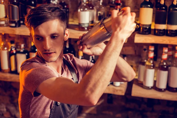 Junger dunkelhaariger Barmann benutzt Shaker bei der Herstellung von Cocktails — Stockfoto