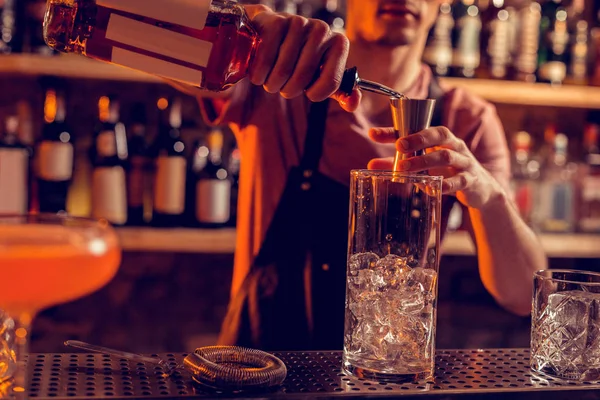 Barman usando uniforme derramando álcool em vidro com gelo — Fotografia de Stock