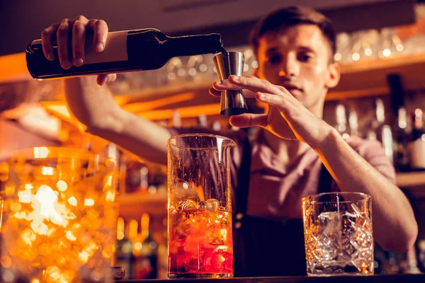 Barman de cabelo escuro adicionando um pouco de álcool ao coquetel — Fotografia de Stock