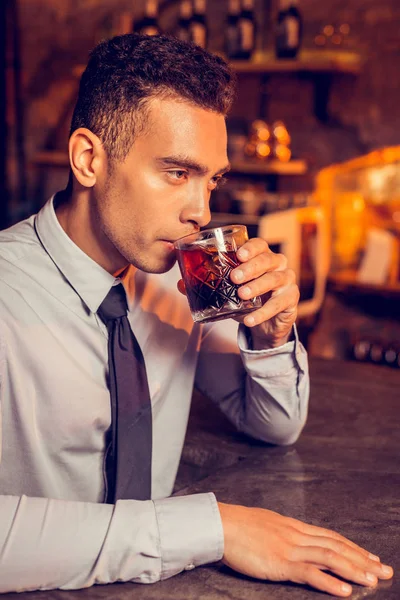 Успешный человек расслабляется, выпивая виски в баре — стоковое фото