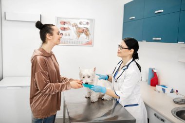 Genç, siyah saçlı bir kadın köpeğini veterinerden aldığı için minnettar.