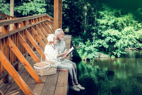 Merry spouses in years sitting outdoors and enjoying a book — Stock Photo, Image