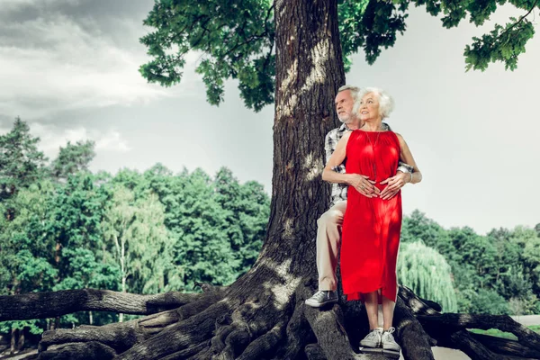 Attractive man tenderly cuddling wife while standing under the tree — Stock Photo, Image