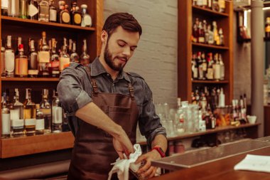Barda yakışıklı koyu saçlı sakallı yetişkin barmen parlatma gözlük
