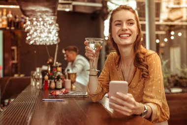 Mutlu kadın elinde telefon ve martini kokteyl tutan