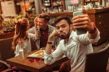 Arkadaşları arka planda sarılırken üzgün erkek selfie çekiyor