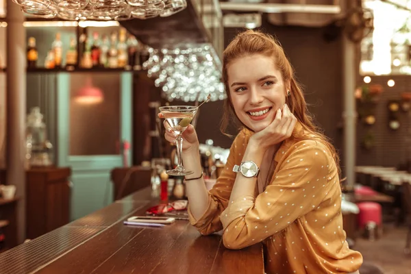 Улыбающаяся женщина с бокалом мартини сидит у барной стойки — стоковое фото