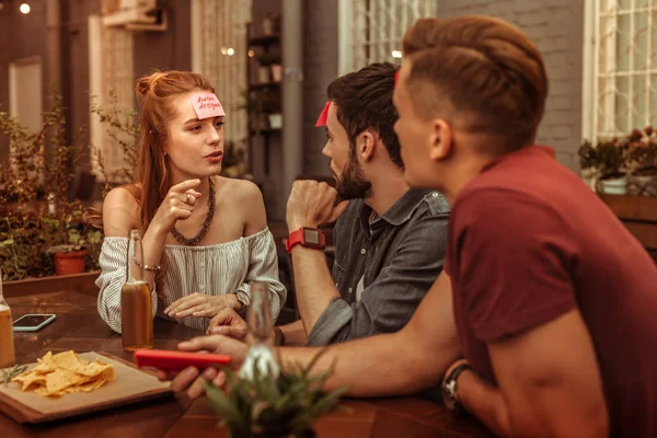 Charmante femme portant un haut blanc jouant à un jeu hedbanz . — Photo