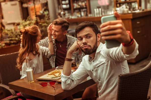 Enojado macho tomando selfies mientras sus compañeros acurrucándose en segundo plano —  Fotos de Stock