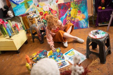 Kıvırcık sanatçı yerde oturan ve onun resimleri bitirme