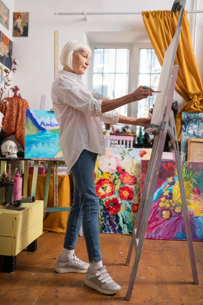 Artista envelhecido vestindo jeans e tênis pintura em oficina — Fotografia de Stock