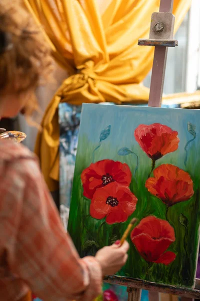 Curly red-haired artist standing near canvas with red poppies — Stock Photo, Image