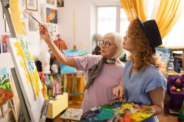 Седовласая учительница рисования в очках разговаривает со своим учеником — стоковое фото