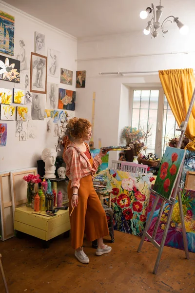 Young artist wearing bright clothes standing near canvas — Stock Photo, Image