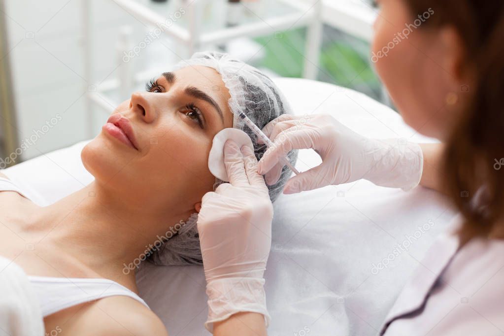 Professional skilled dermatologist doing forehead botox injections
