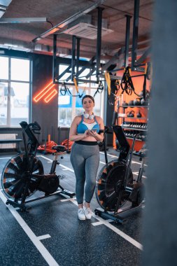 Dolgun kadın spor salonunda egzersiz döngüsü yakınında ayakta