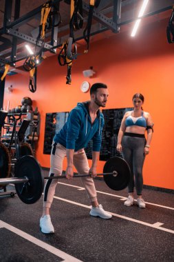 Yakışıklı eğitmen müvekkilinin yanında barbell ile çalışıyor