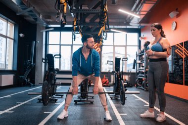 Koyu saçlı eğitmen, müvekkiline bunu gösteren barbell kaldırıyor