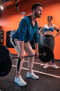 Sakallı eğitmen müşteri ile çalışmadan önce barbell ile çalışma