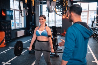 Kadın eğitmen yanında duran barbell kaldırdıktan sonra gülümseyen