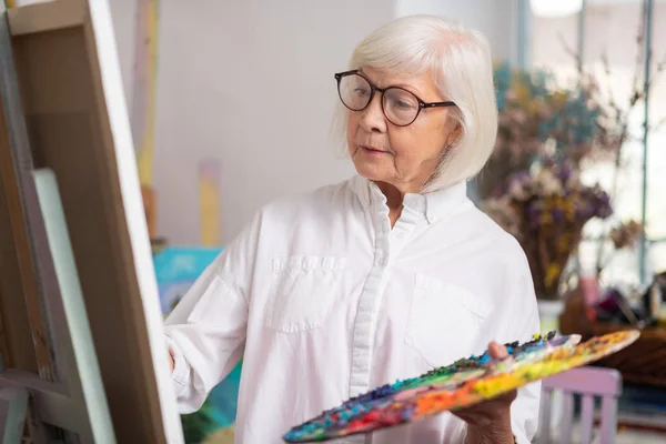 Talented retired woman painting standing near canvas — Stock Photo, Image