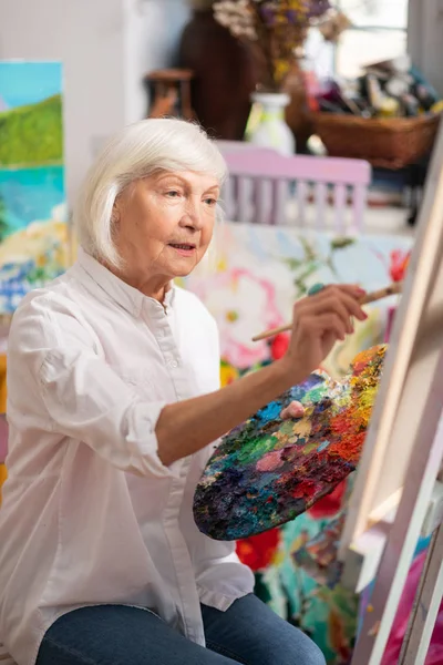 Vista superior de una mujer anciana sentada cerca de un lienzo con paleta de colores —  Fotos de Stock