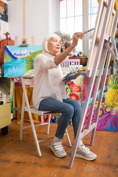 Mulher vestindo tênis elegantes sentado perto de tela e pintura — Fotografia de Stock