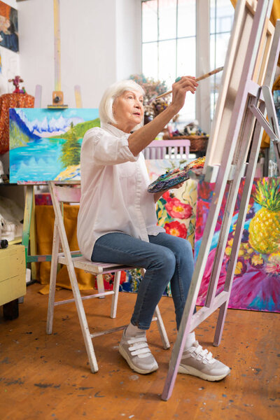 Woman wearing stylish sneakers sitting near canvas and painting