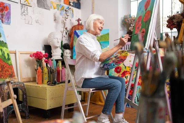 Artista envelhecido sentindo-se verdadeiramente satisfeito enquanto pinta papoilas vermelhas — Fotografia de Stock