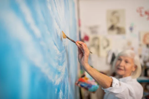 Aged artist holding painting brush and coloring canvas — Stock Photo, Image