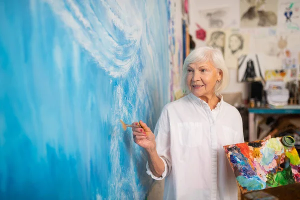 Καλλιτέχνης στέκεται κοντά σε μεγάλο καμβά και χρωματίζοντας το σε μπλε — Φωτογραφία Αρχείου