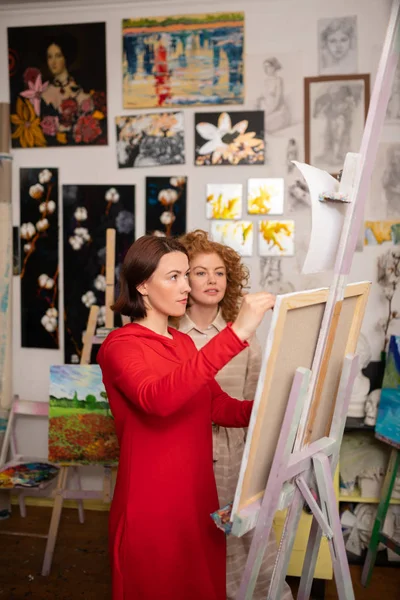 Artist painting on canvas standing near her friend — Stock Photo, Image