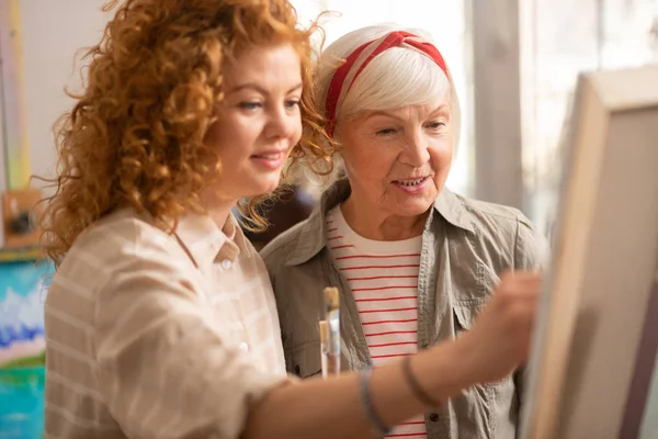 Grauhaarige, gealterte Kunstlehrerin steht neben ihrer talentierten Schülerin — Stockfoto