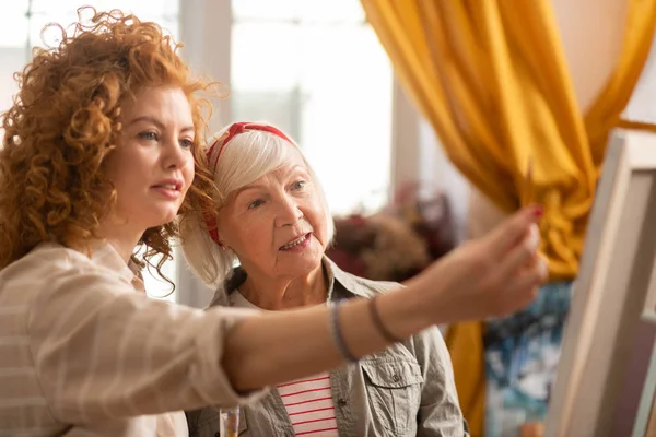 Grey-haired art tutor talking to her student drawing on canvas — Stock Photo, Image