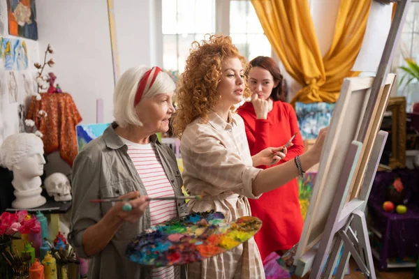 Aged teacher looking at her student drawing on canvas — Stock Photo, Image