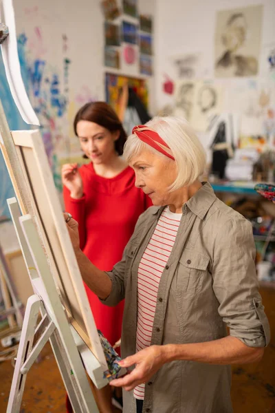 Aged famous artist painting near her dark-haired student — Stock Photo, Image