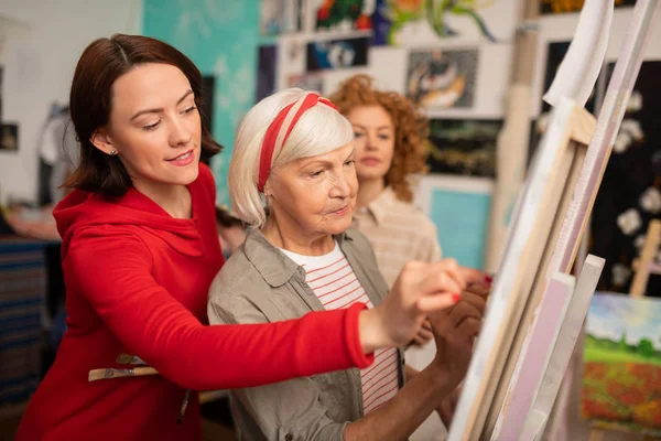 Aged art teacher and her students helping her drawing on canvas — Stock Photo, Image