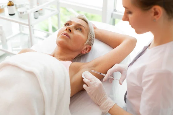 Serious grey haired woman having a painful procedure — Stock Photo, Image