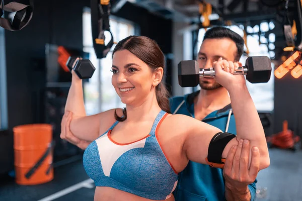 Entrenador ayudando a la mujer positiva haciendo ejercicios para los brazos — Foto de Stock