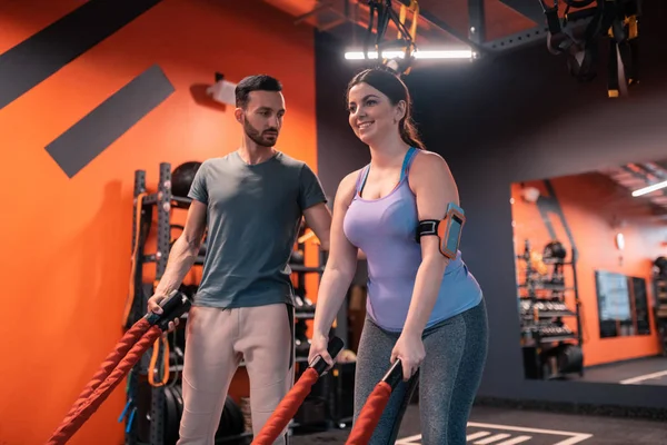 Eğitmen egzersiz için Trx kayışları kullanarak yağlı kadın yardım