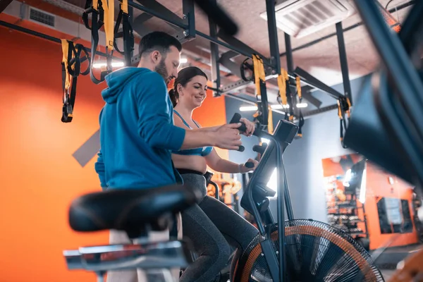 Kilolu kadın spor salonunda bisiklet gülümseyen ve eğitmen konuşuyor