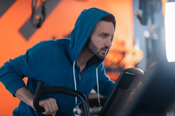 Dark-haired athletic man feeling thoughtful while cycling in gym