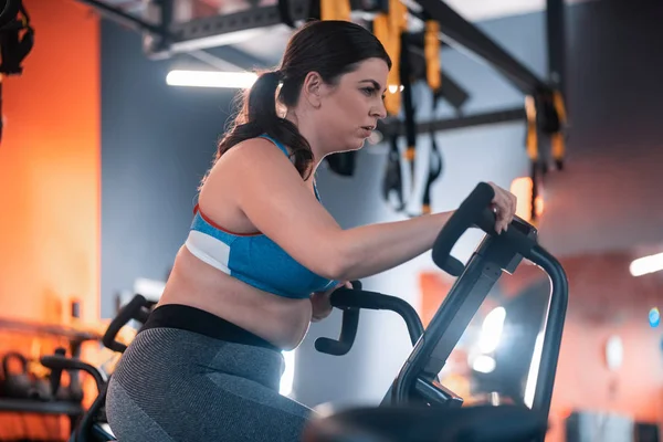 Mujer regordeta ciclismo en el gimnasio sintiéndose realmente agotado — Foto de Stock